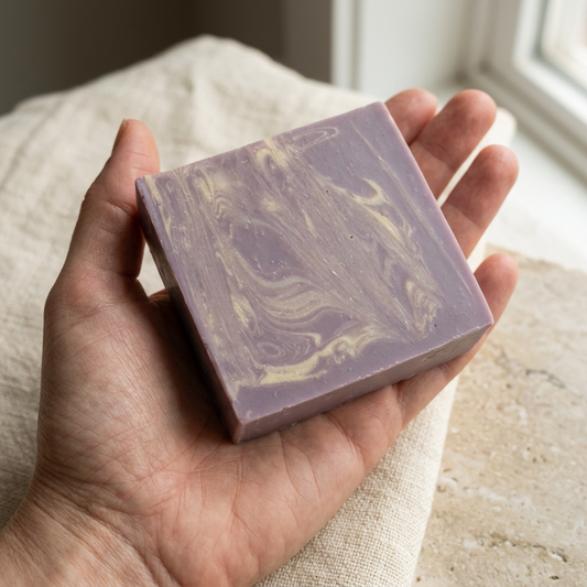 Lavender & Vanilla soap resting in an open palm, showing its cream swirls, handmade texture and bar thickness.